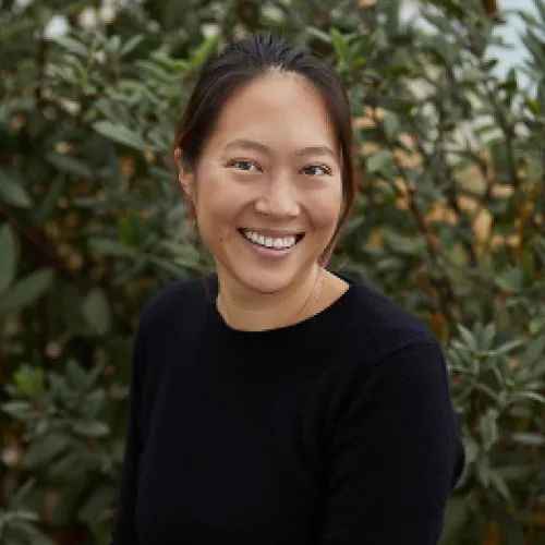 A woman smiling in front of bushes.