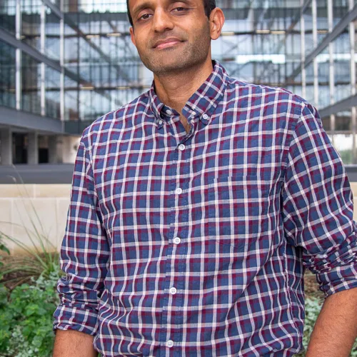 A man in a plaid shirt standing in front of a building.