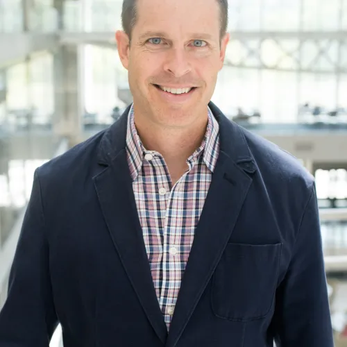 A man in a blue blazer smiling in an office.